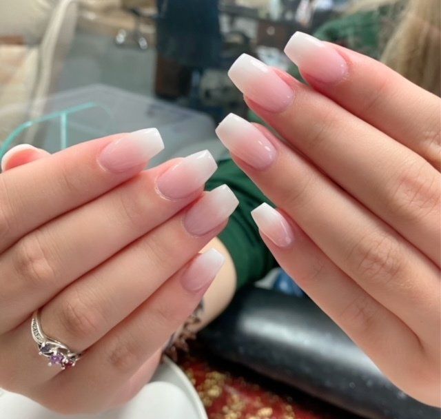 Hands with French ombre square-shaped nails, a ring with a purple stone.