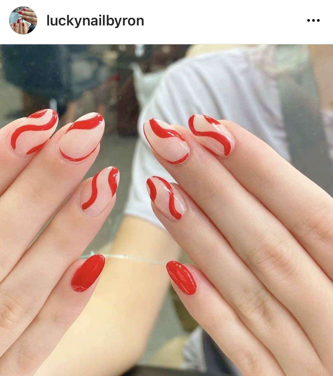 Hands with oval-shaped nails. Some are clear with red wavy lines, others are solid red.