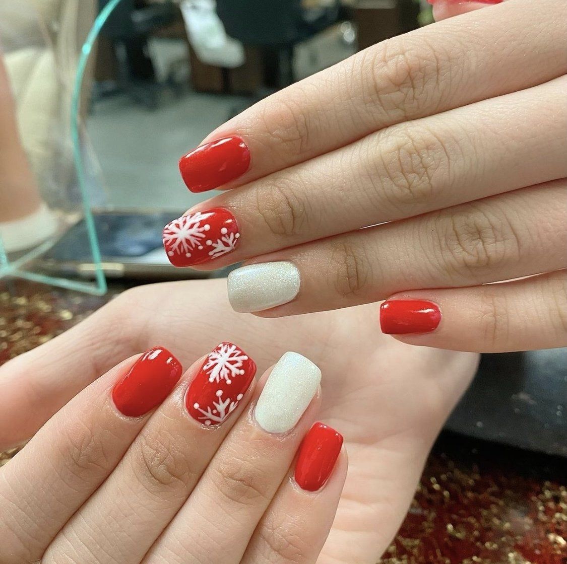 Hands with red and white Christmas-themed nail art: snowflakes and glitter.
