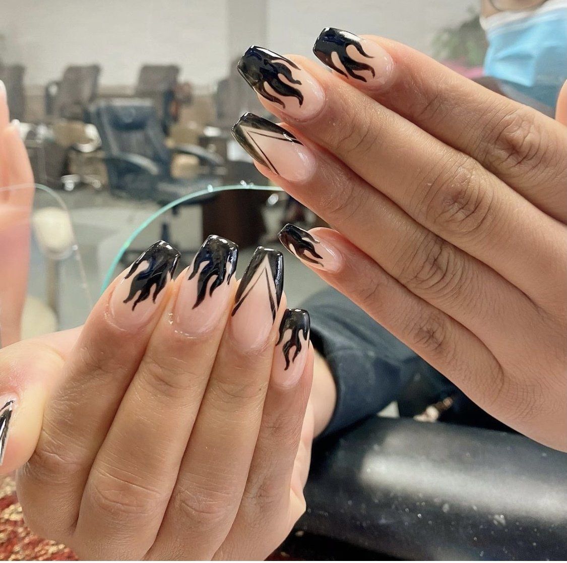Hands with flame-design nail art: black flames on a neutral nail base, in a salon setting.