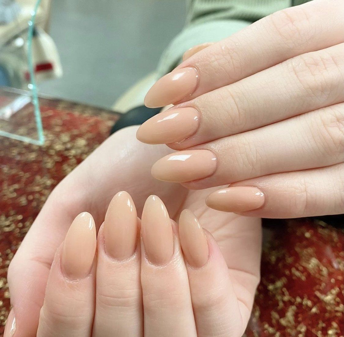 Hands with almond-shaped nails painted a light, neutral beige.