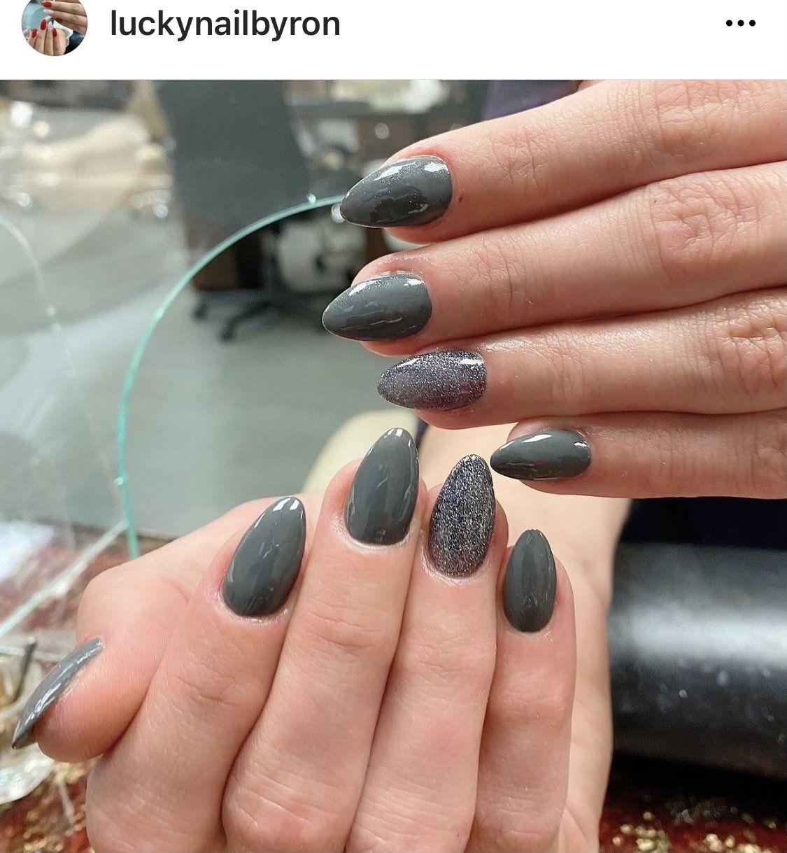 Hands with gray and glitter gel-polished almond-shaped nails, with a reflection in a mirror.