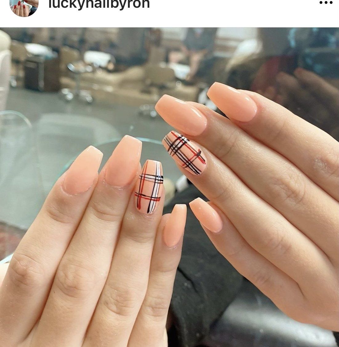Hands with peach-colored coffin-shaped nails, one accent nail with a plaid design.