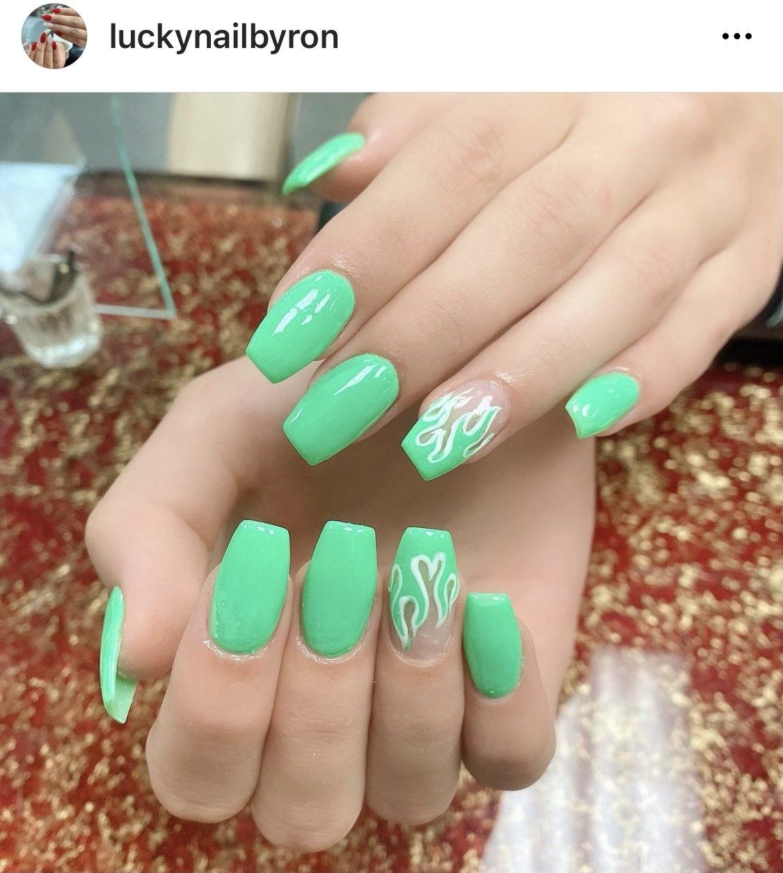 Green coffin-shaped nails with flame design on the ring fingers.