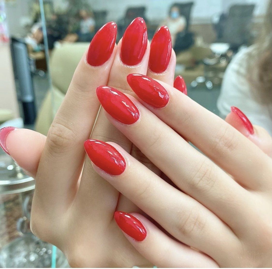 Hands with almond-shaped nails painted glossy red, indoors.