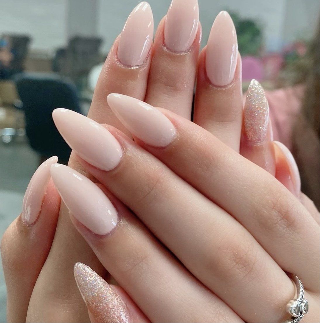 Hands with almond-shaped, light pink nails, one with glitter.