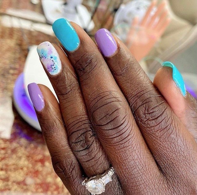 Hand with a manicure in shades of blue, purple, and white.
