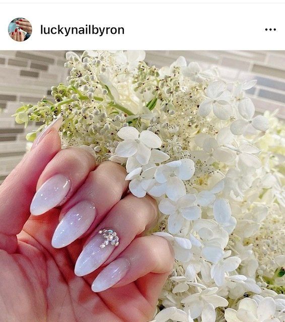 Hand holding white flowers, showing white, oval-shaped nails with a jewel accent.