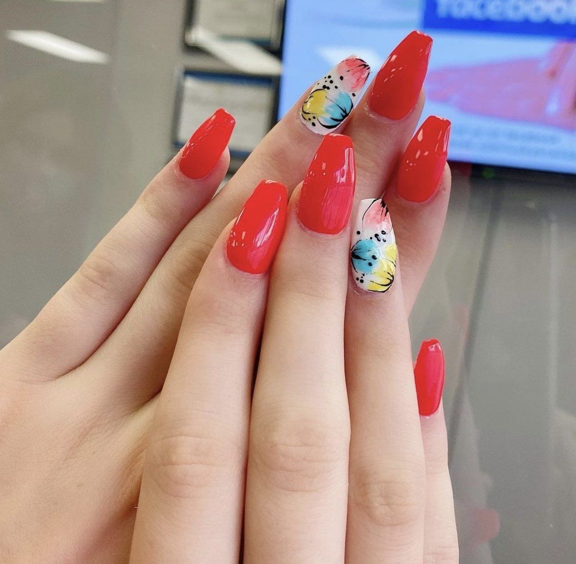 Hands with long, red acrylic nails; two nails have colorful butterfly designs.