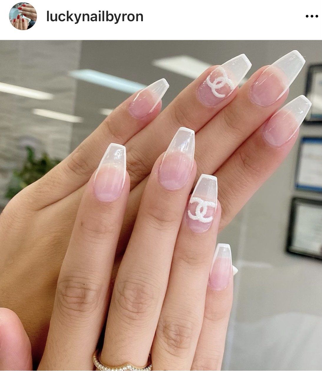 Hands with long, clear acrylic nails, French tips, and Chanel logo accents; diamond ring.