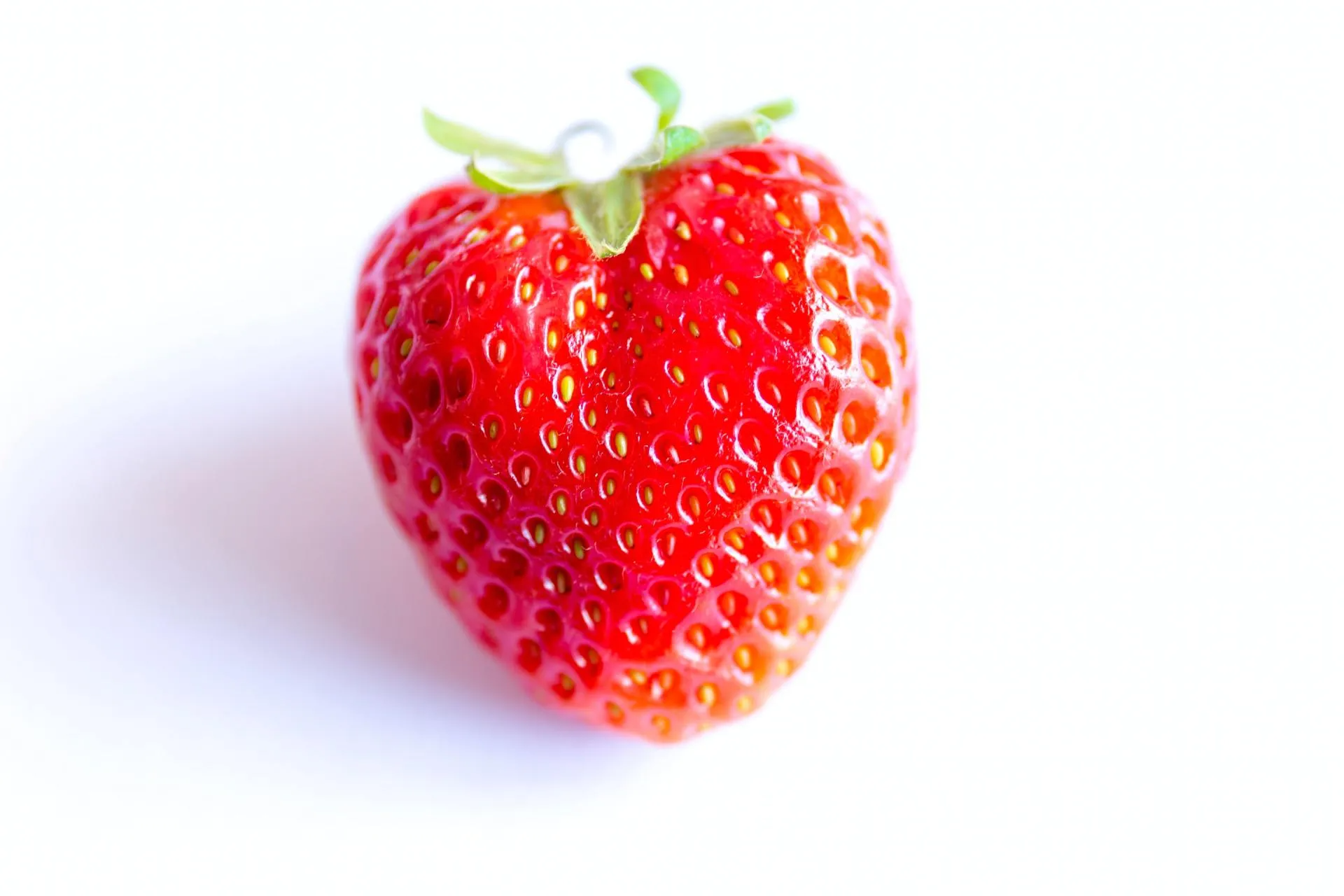 A single strawberry is sitting on a white surface.