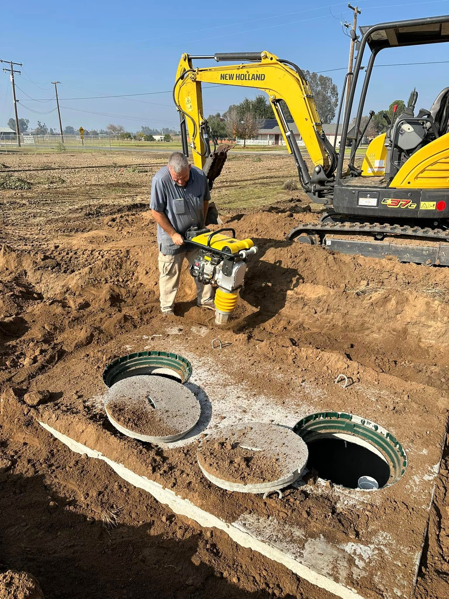 A man is standing in the dirt next to a yellow excavator.