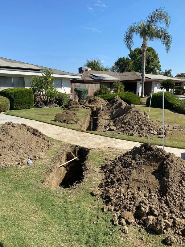 Trenches dug in a suburban lawn, piles of dirt, residential homes in the background, sunny day.