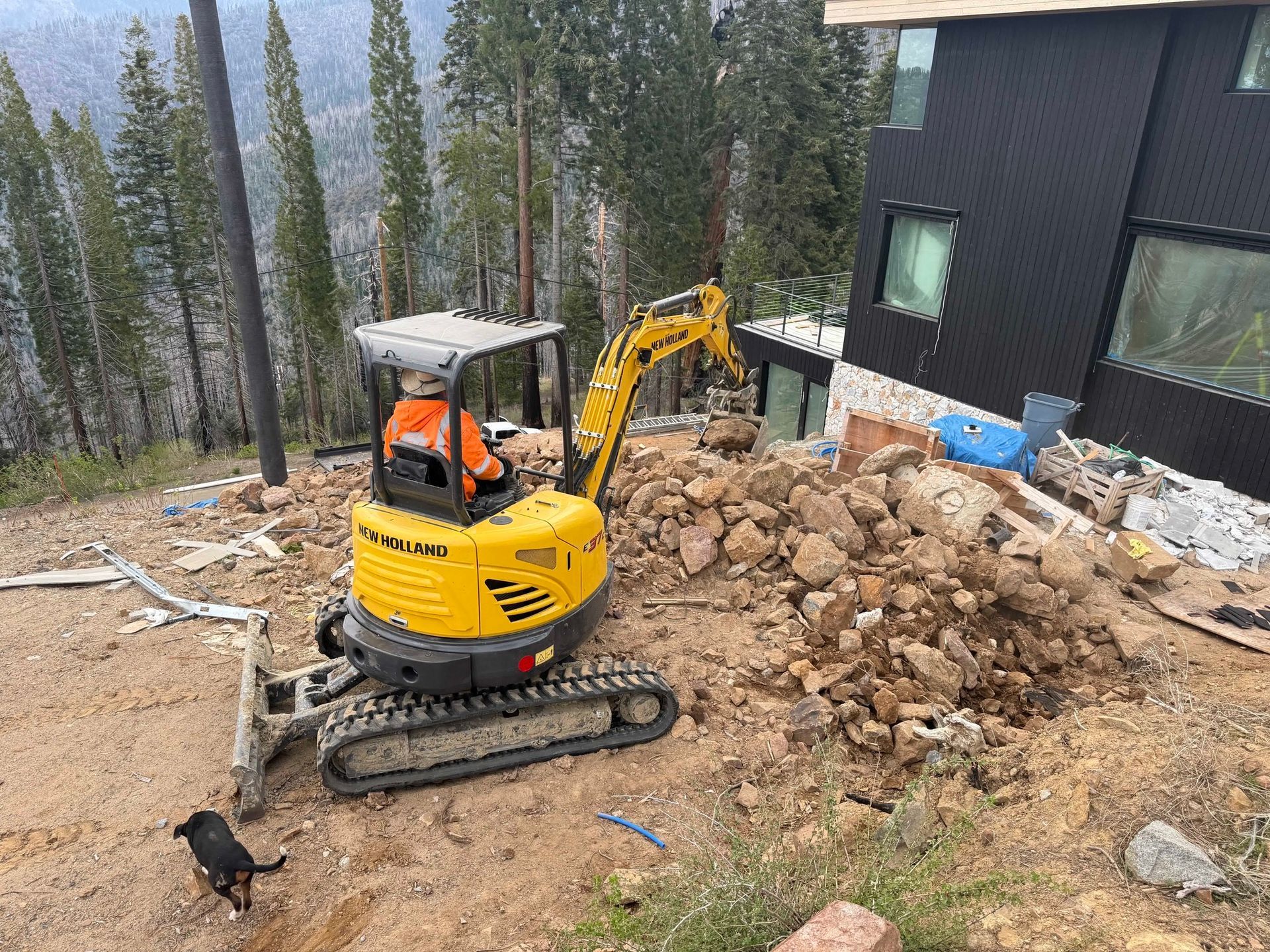 A yellow excavator is sitting on top of a pile of rocks in front of a house.
