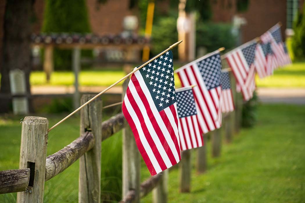 A row of american flags hanging on a wooden fence.