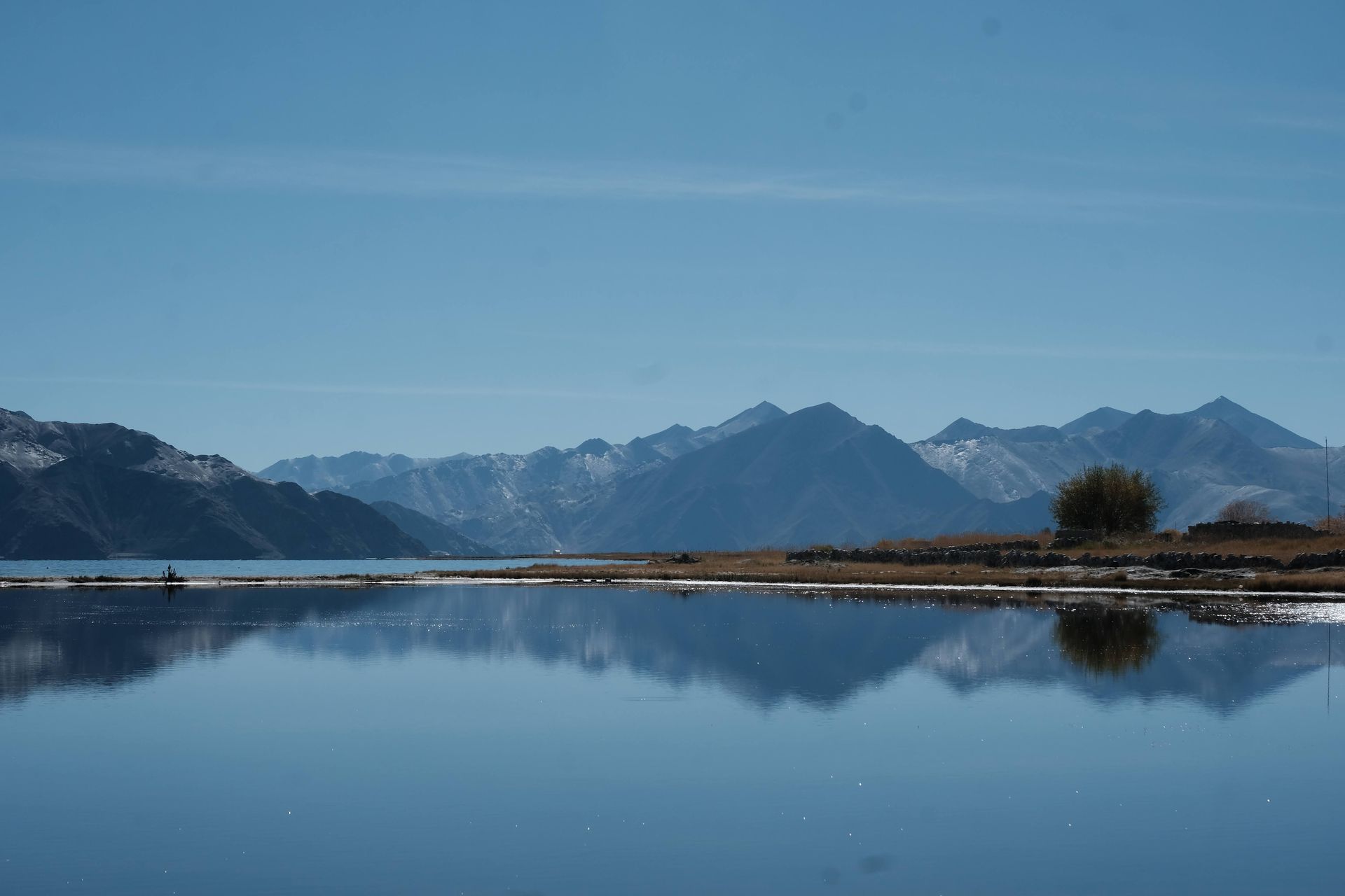 Calm lake reflecting snow-capped mountains and a clear blue sky.