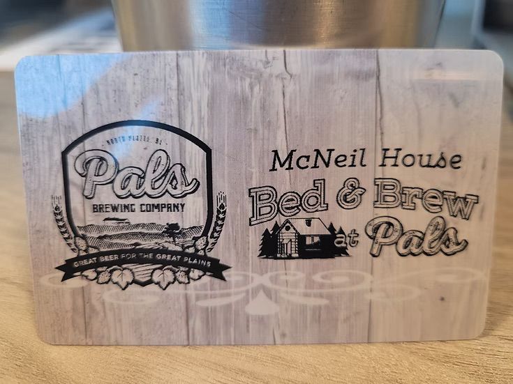 Credit card-like sign for "McNeil House Bed & Brew Pals" with brewery logo on woodgrain background.