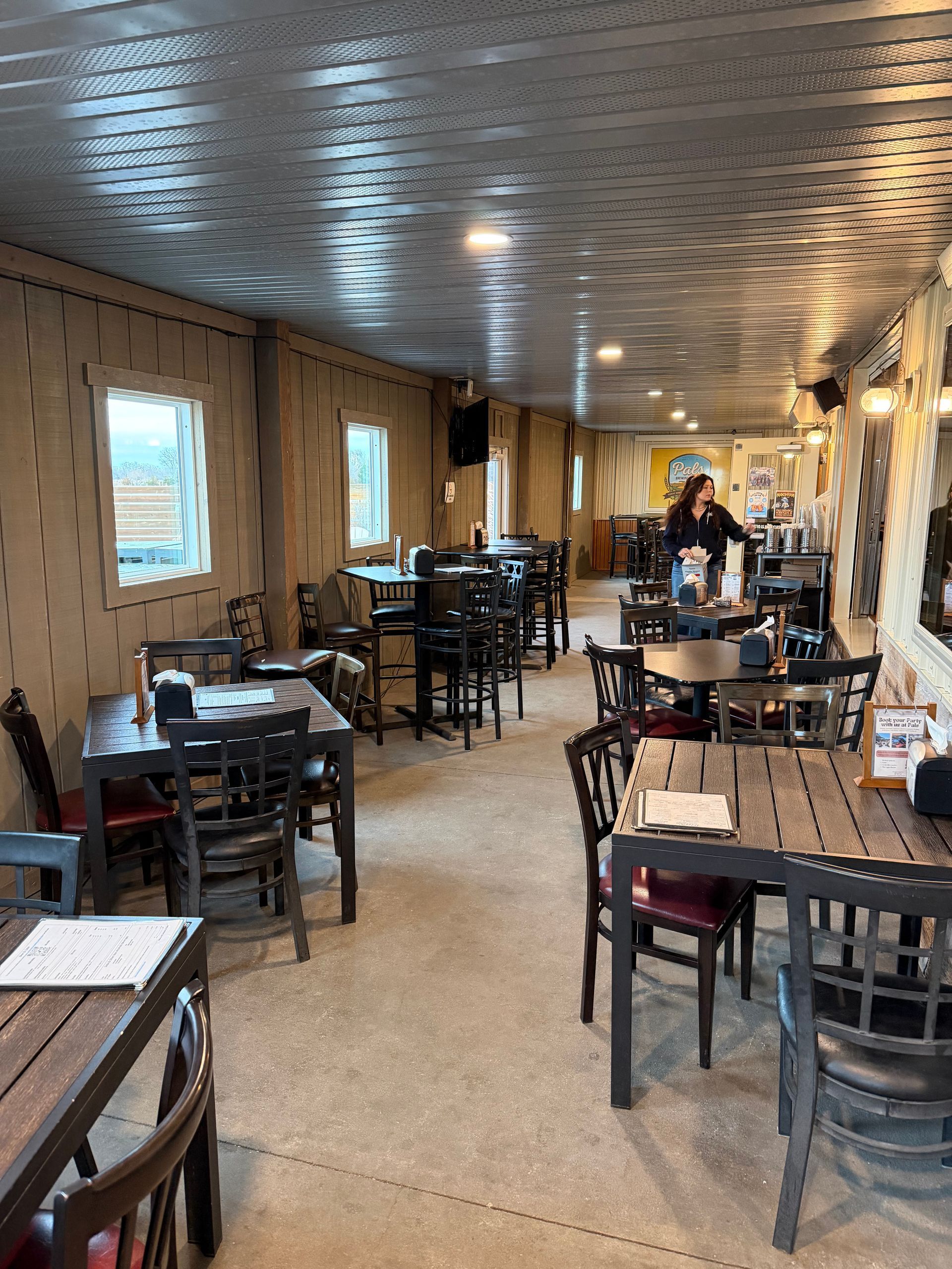 Aerial view of an outdoor event. People gather at a venue with a long white tent, food trucks, and a large parking area.