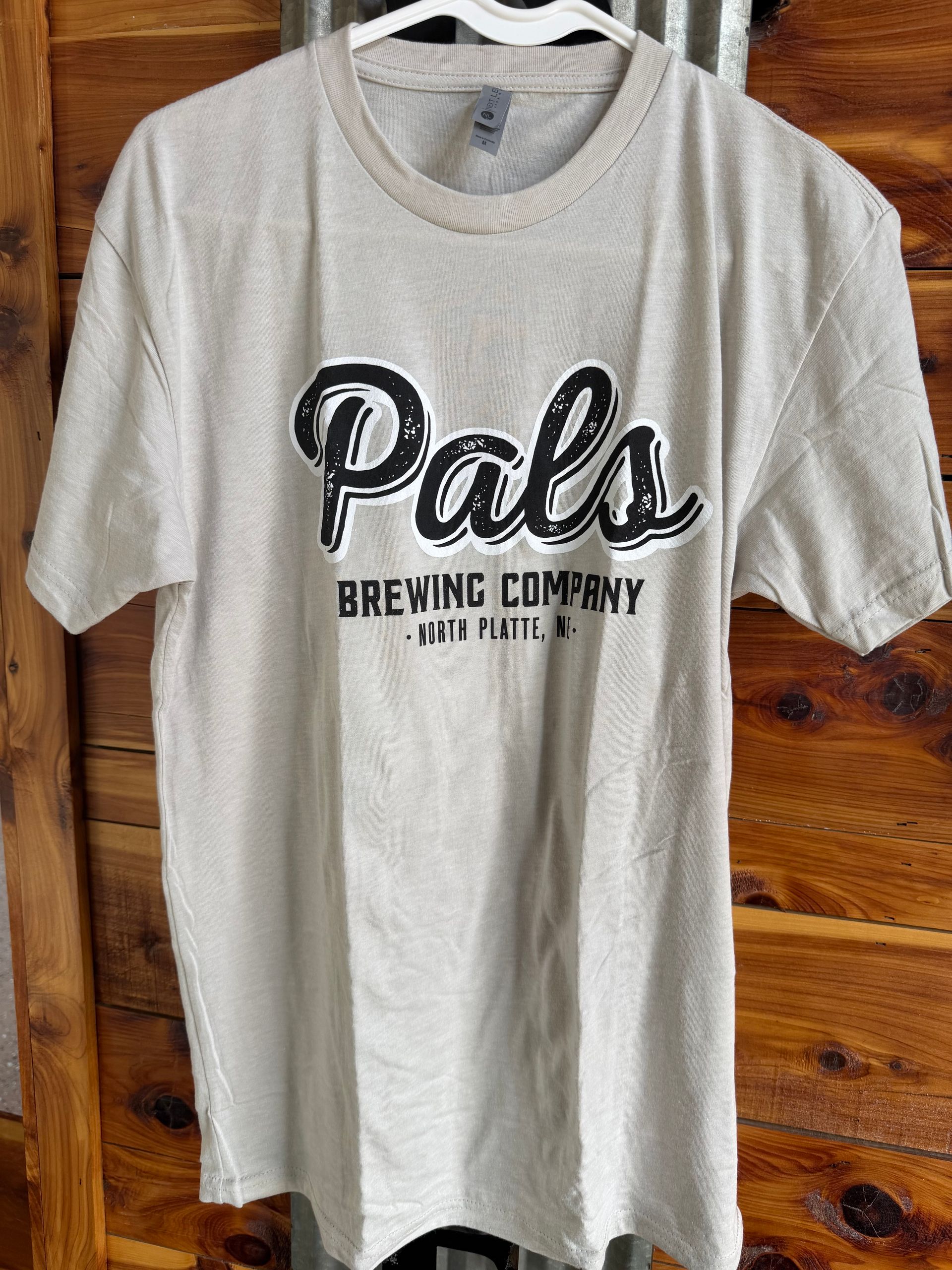 Tan t-shirt with "Pals Brewing Company" logo in black script on a wooden background.