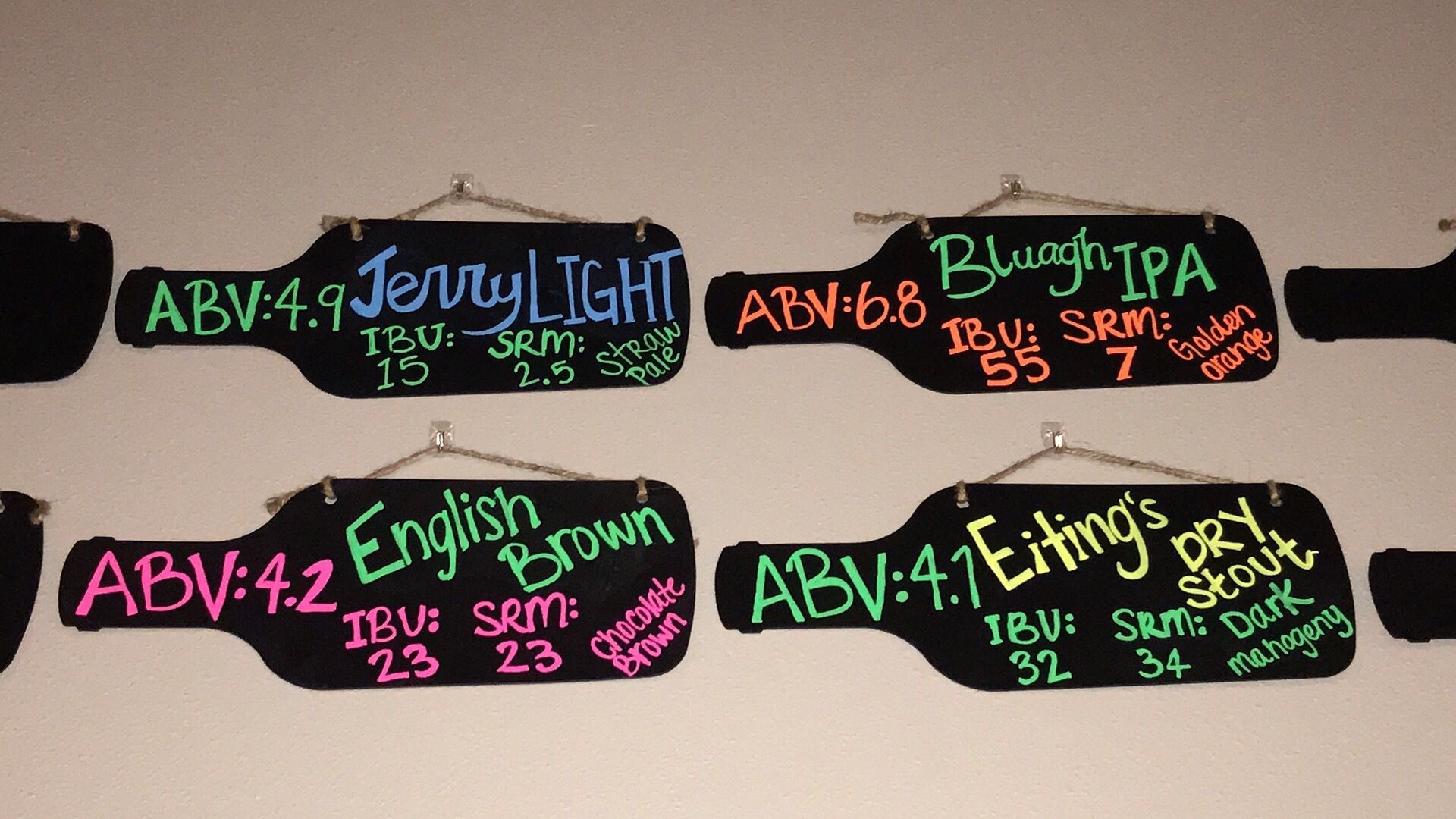 Beer menu signs shaped like bottles on a wall, listing ABV, IBU, and SRM of different beers.