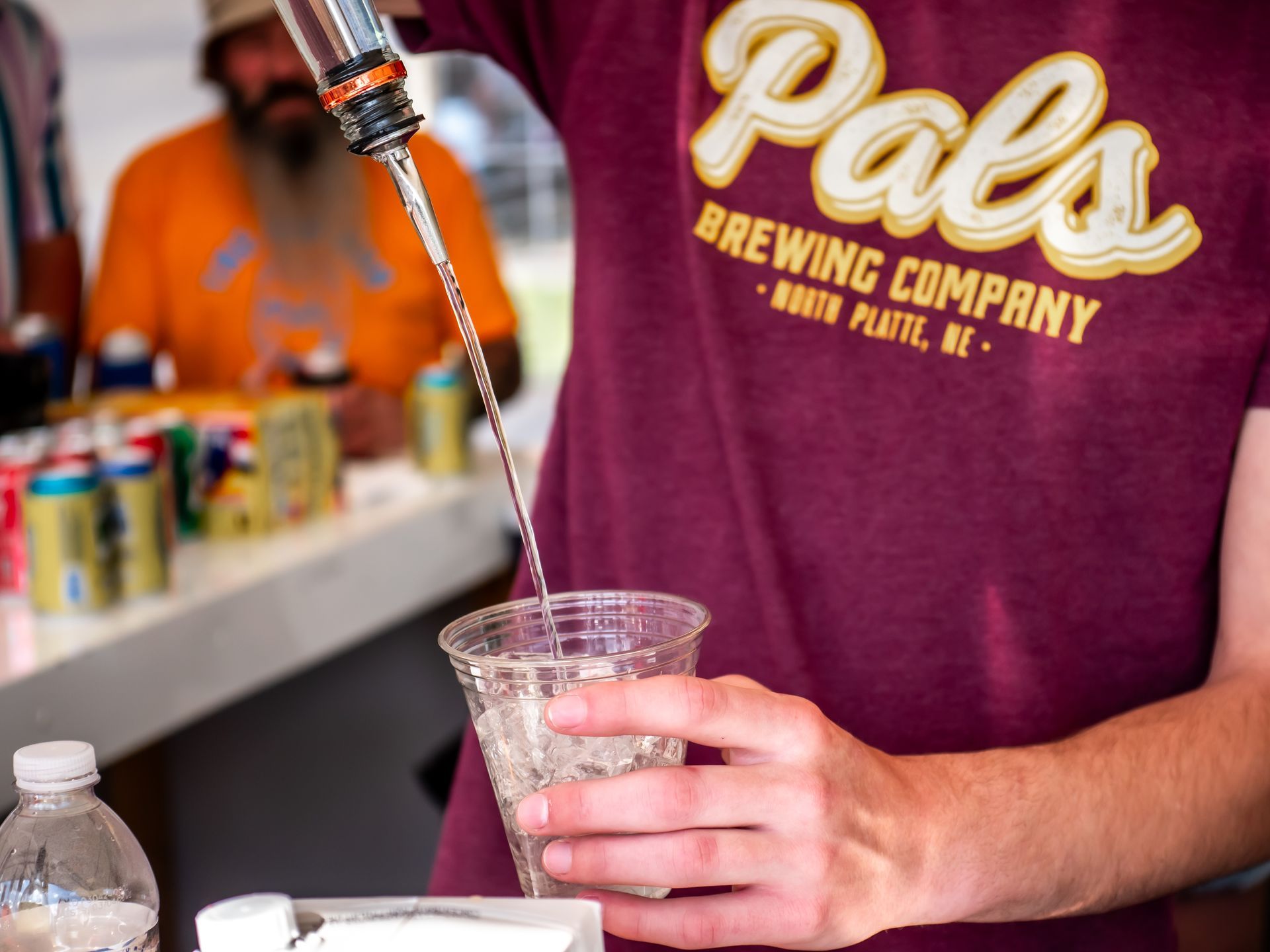 Person pouring liquid from a bottle into a clear plastic cup. 