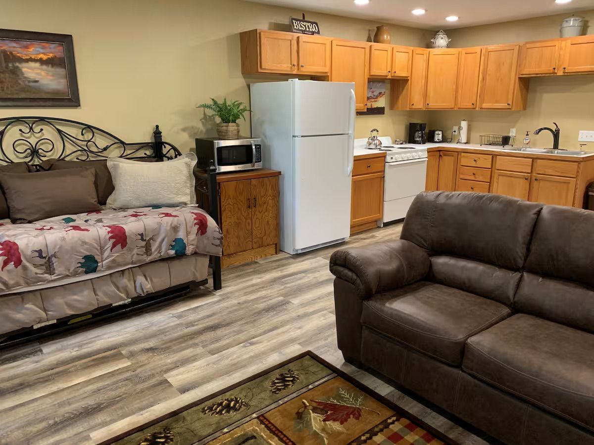 Cozy, furnished apartment with a daybed, kitchen, and brown leather couch.