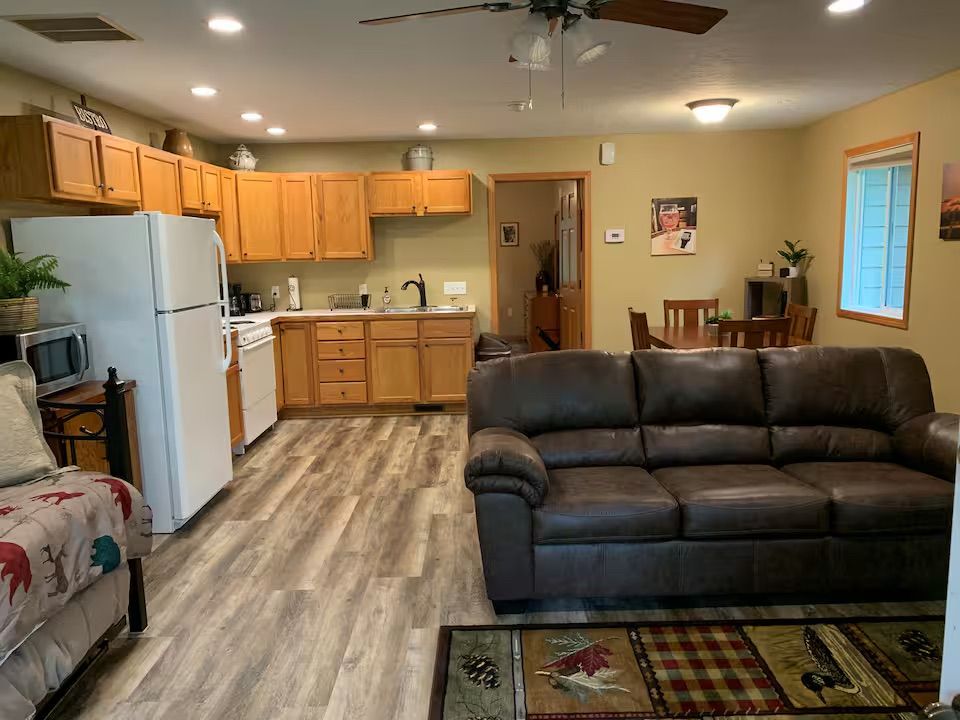 Open-concept kitchen and living area with wooden cabinets, white appliances, and a brown leather sofa.