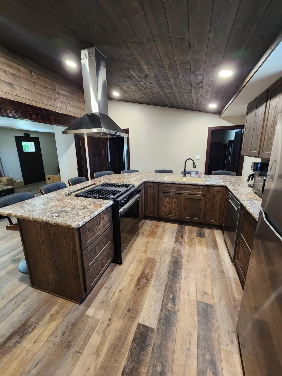 A kitchen with wooden cabinets, countertops, and flooring. Stainless steel range hood above a stovetop on an island.
