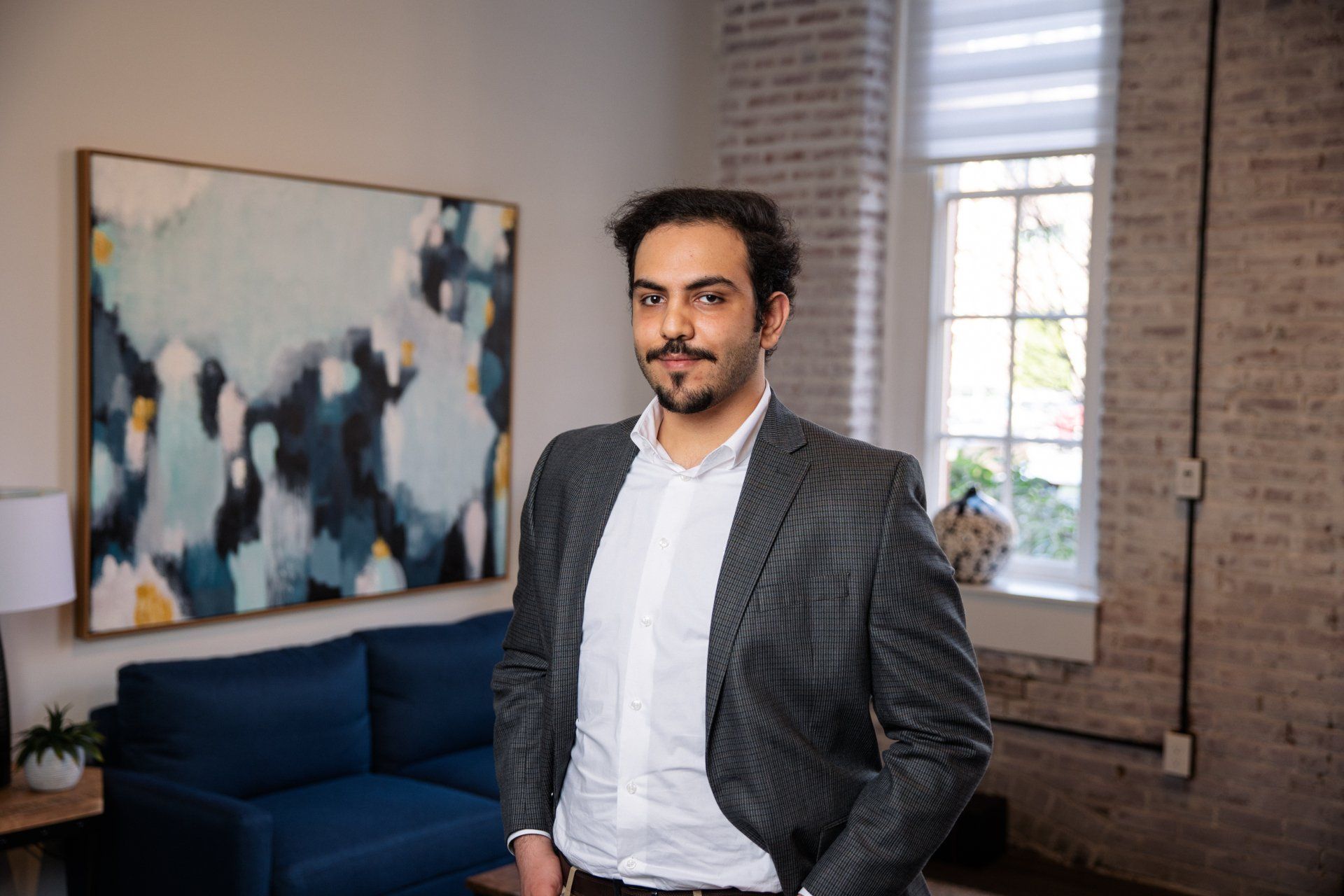 Man standing in a bright office with a blue couch, abstract painting, and window light