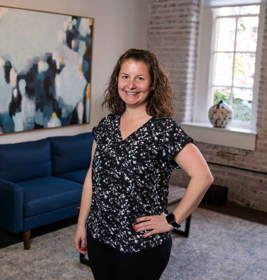 Woman standing in a bright living room, smiling beside a blue sofa and abstract wall art.