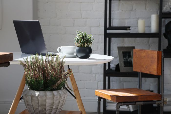 Bright café patio with a laptop, coffee cup, and potted plants by a white brick wall