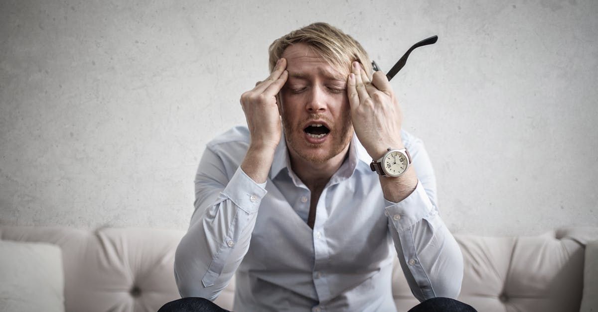 A man is sitting on a couch with his hands on his head.