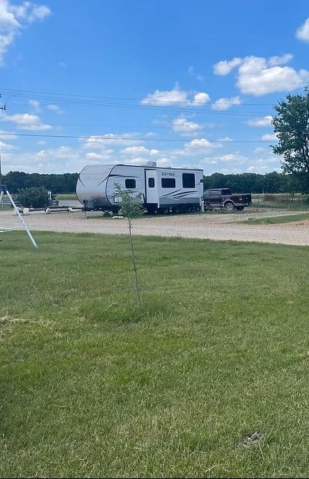 A white travel trailer parked on a gravel lot under a bright blue sky.