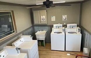 A laundry room with three white washing machines, a utility sink, a wall cabinet, and a ceiling fan.
