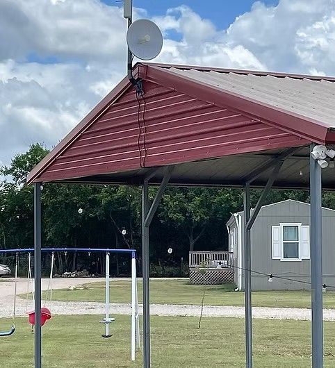 A small parabolic antenna mounted on the corner of a metal-roofed structure next to a yard with a swing set.