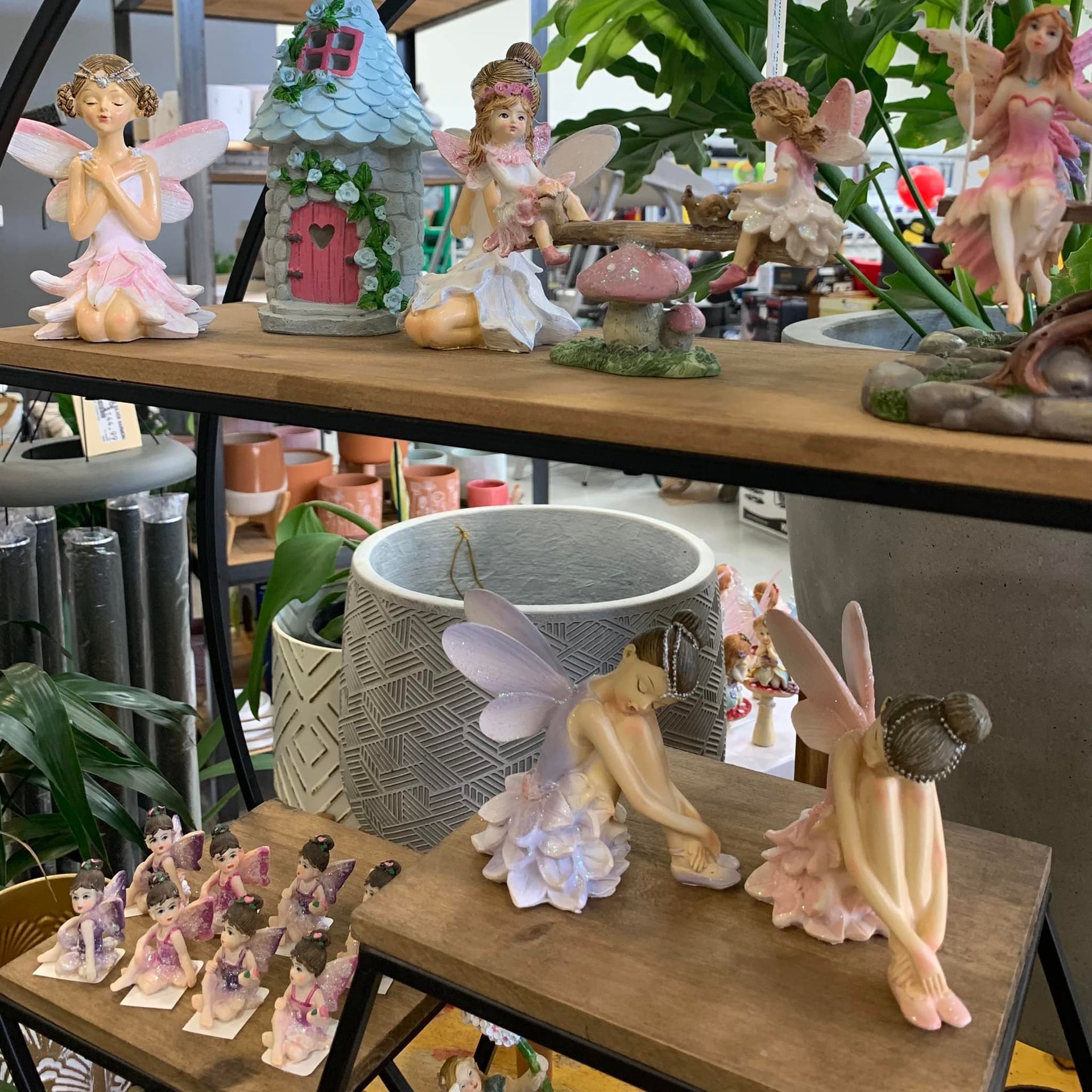 A bunch of fairy figurines are sitting on a wooden shelf.