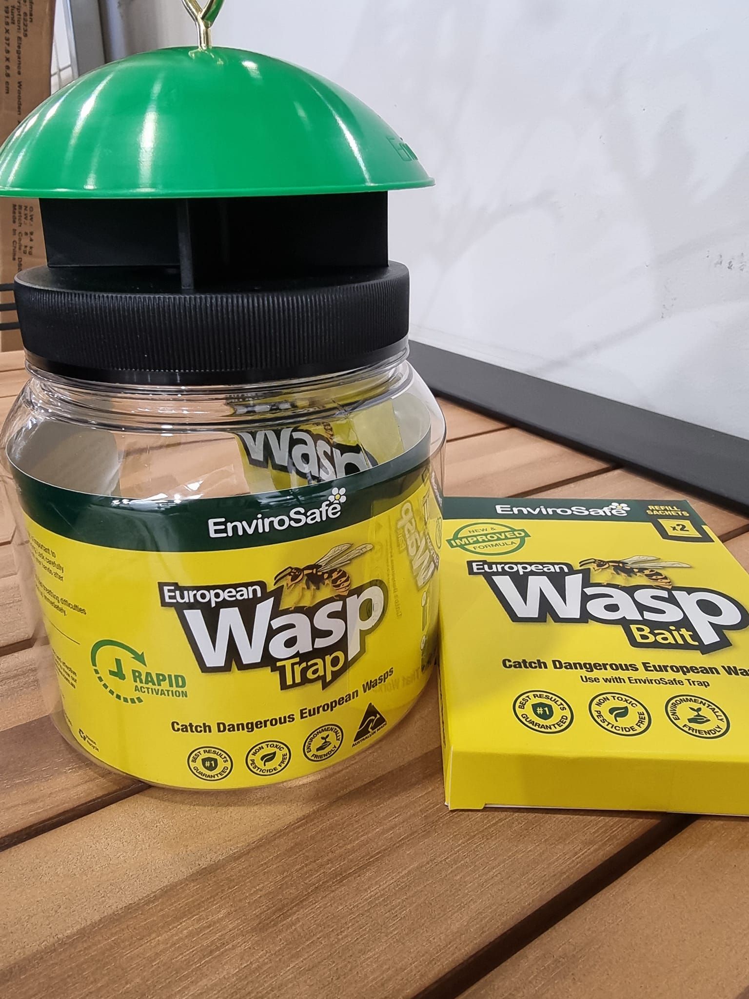 A wasp trap is sitting on a wooden table next to a box of wasp bait.