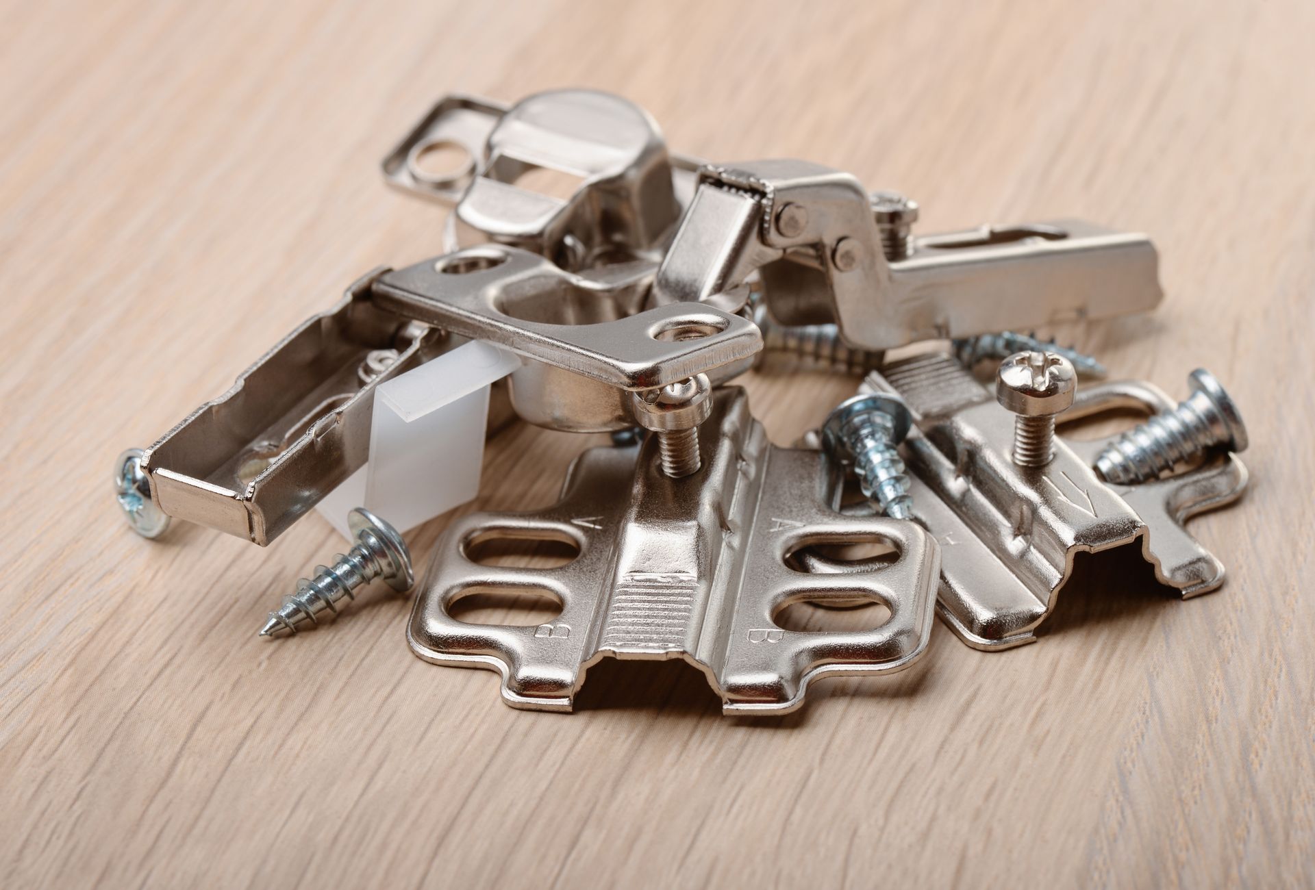 A pile of metal hinges and screws on a wooden table.