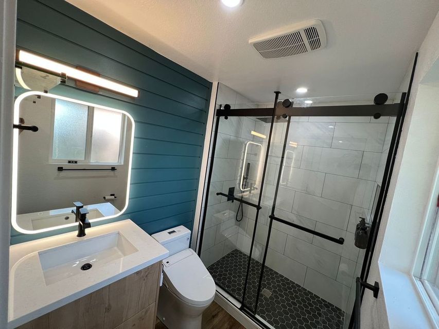 A bathroom with a toilet , sink , mirror and shower.