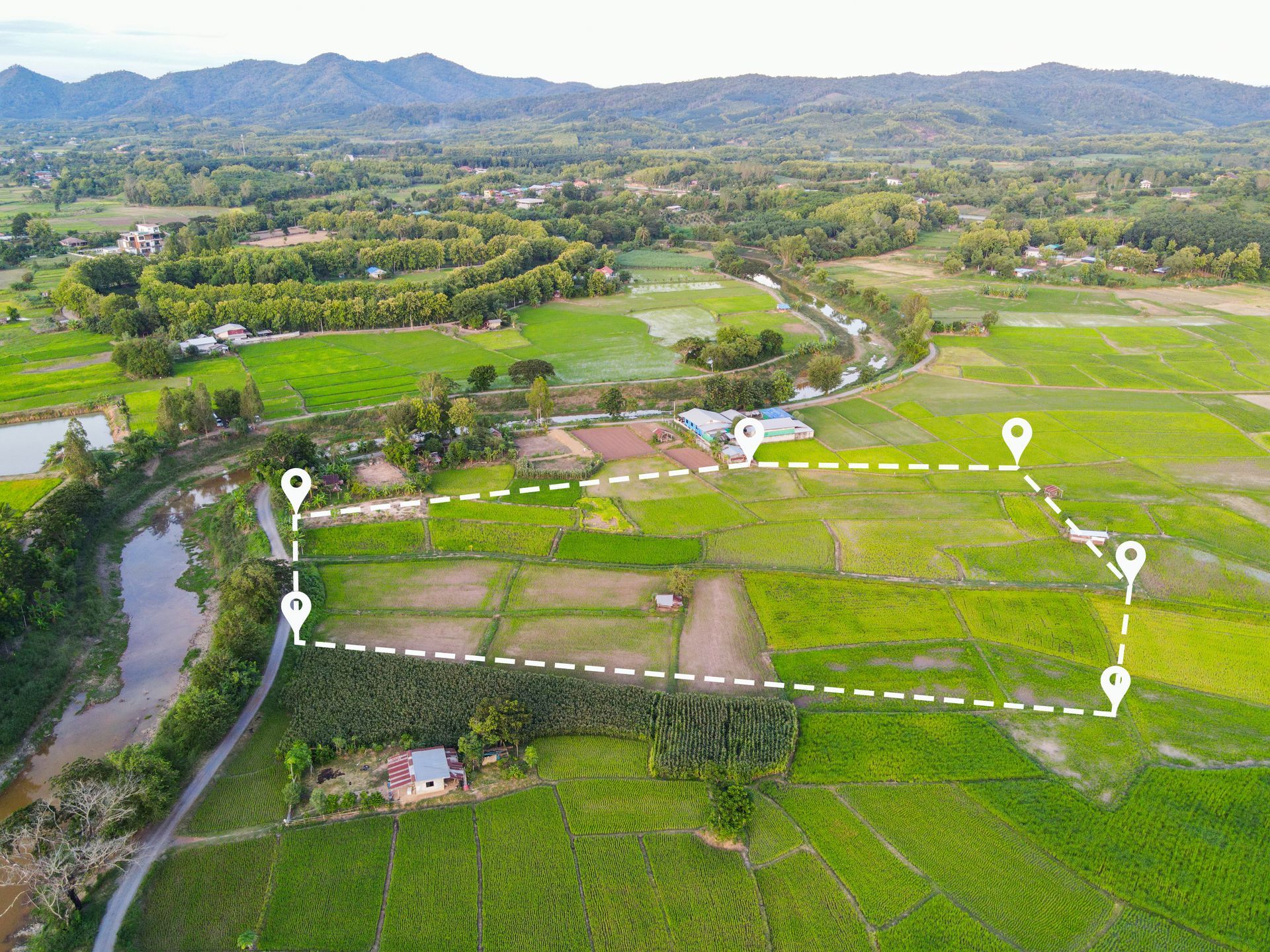 An aerial view of a lush green field with a road and mountains in the background.