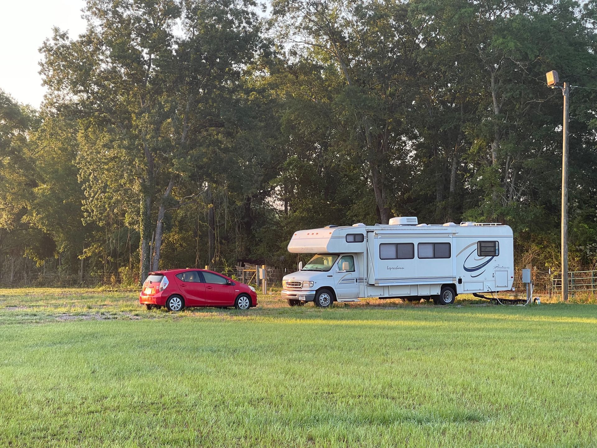 A red car is parked next to a white rv in a grassy field.