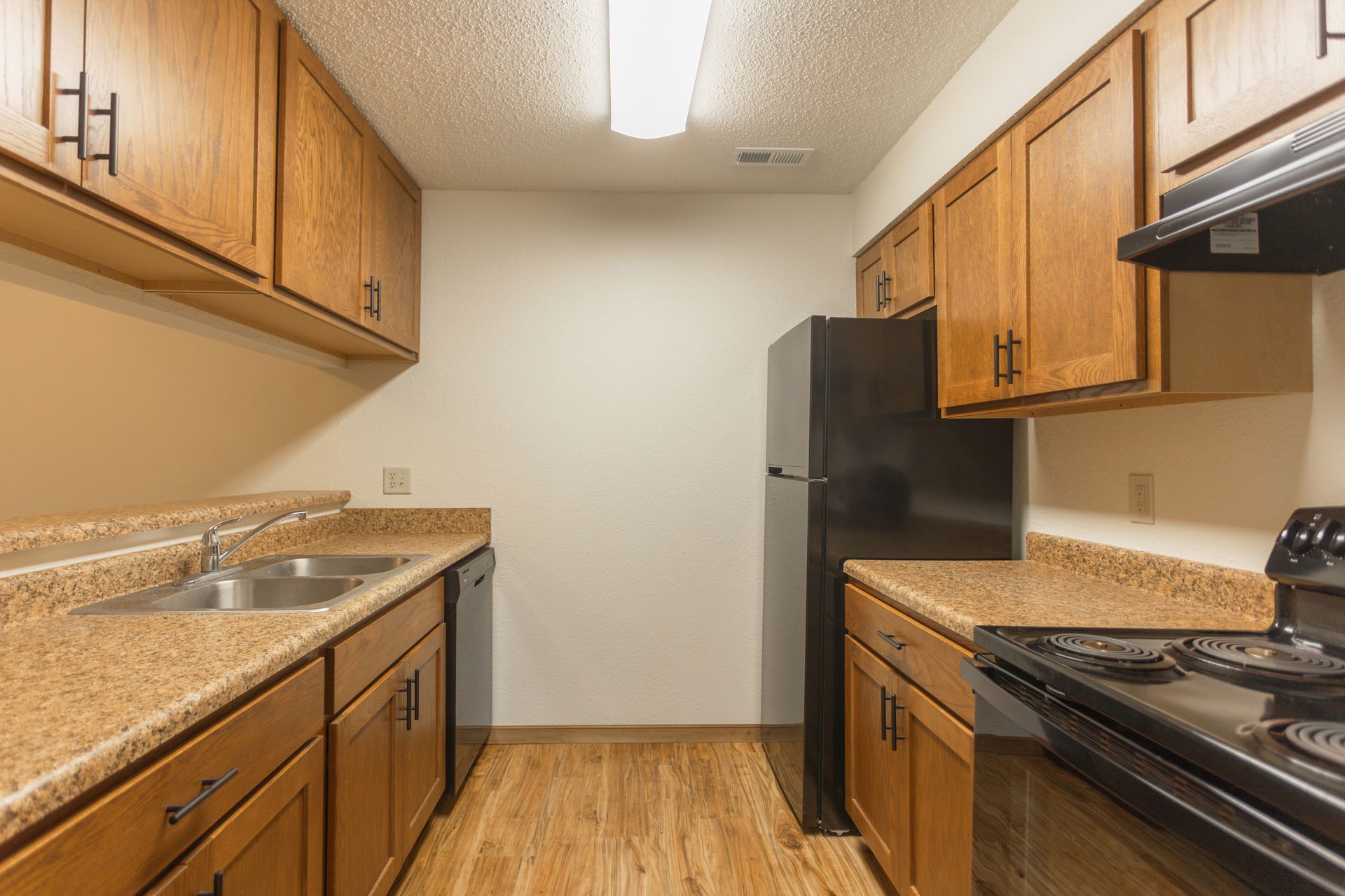 A kitchen with wooden cabinets , a black refrigerator , a stove , and a sink.