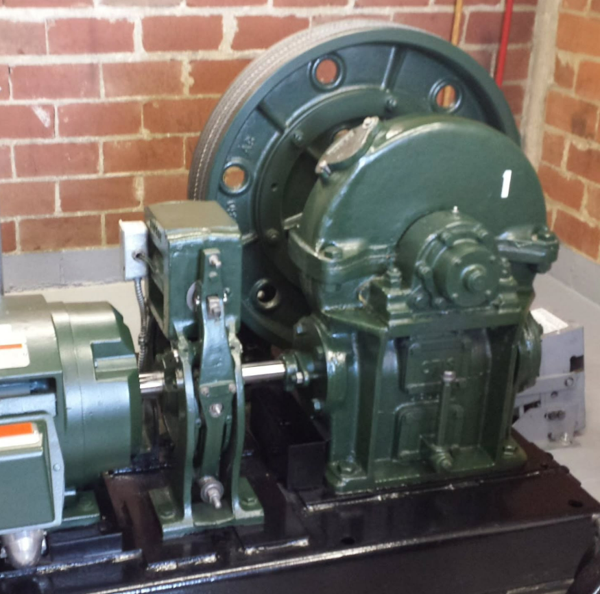 Green industrial machinery mounted on a black base, against a brick wall.