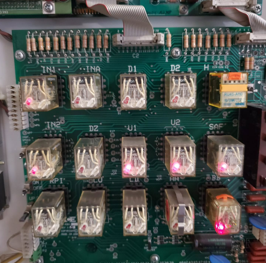 Printed circuit board with multiple relays, some with lit indicator lights, and various electronic components.