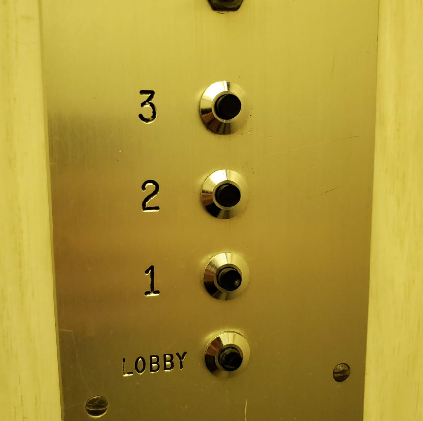 Elevator control panel with buttons for floors 1, 2, 3, and lobby, on a metal panel.