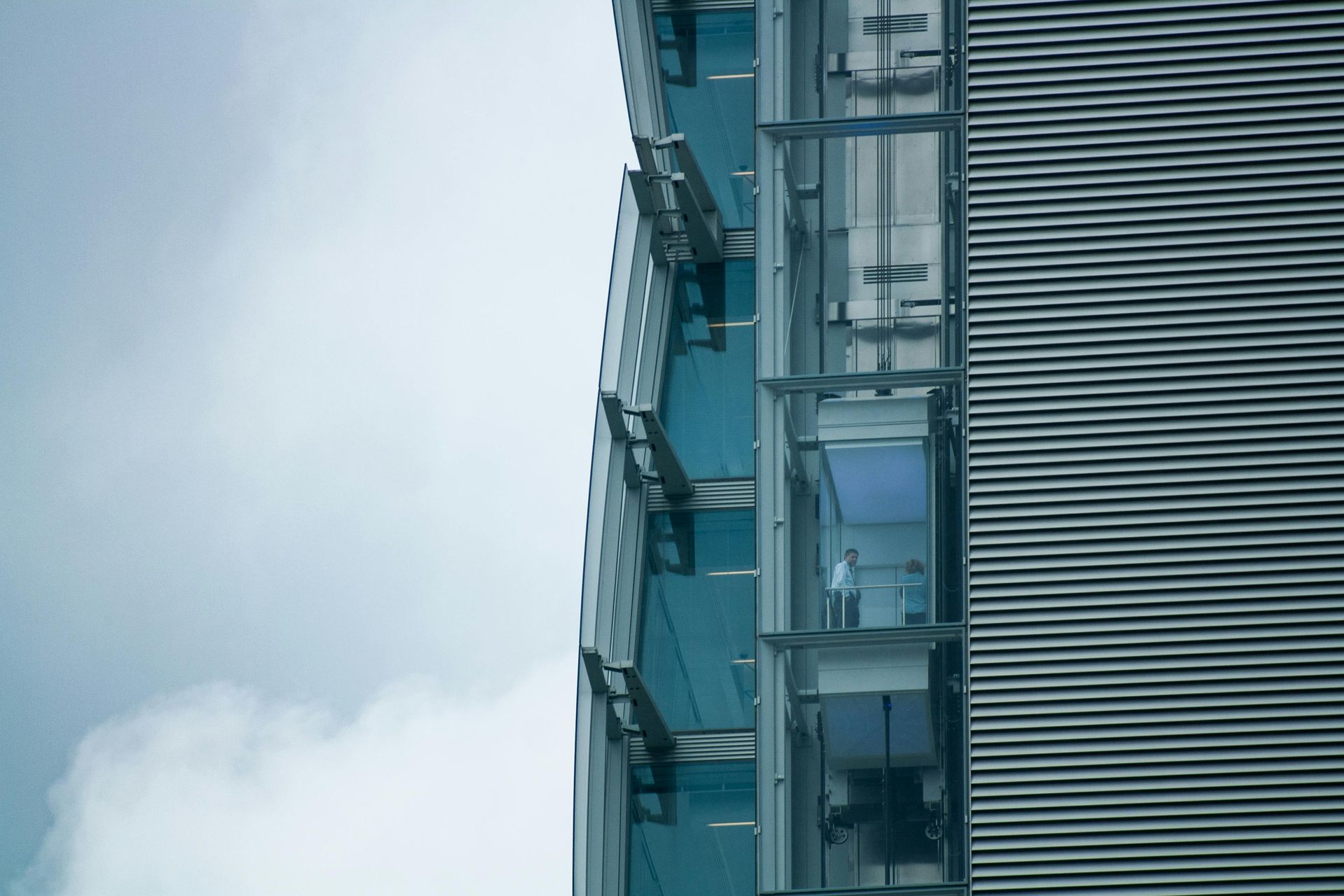 Modern glass and metal office building against a cloudy sky.