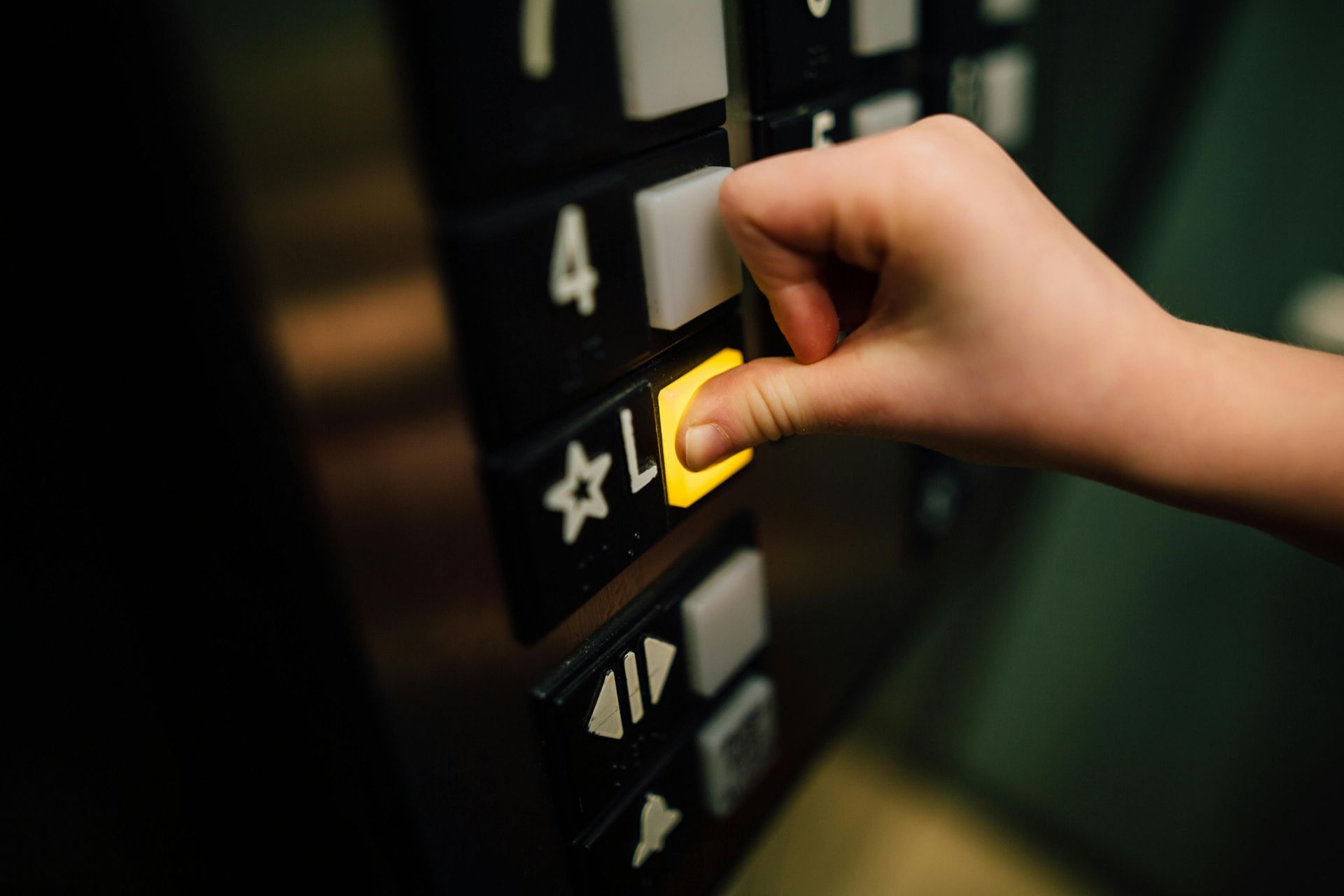 A child's hand presses a lit elevator button labeled 