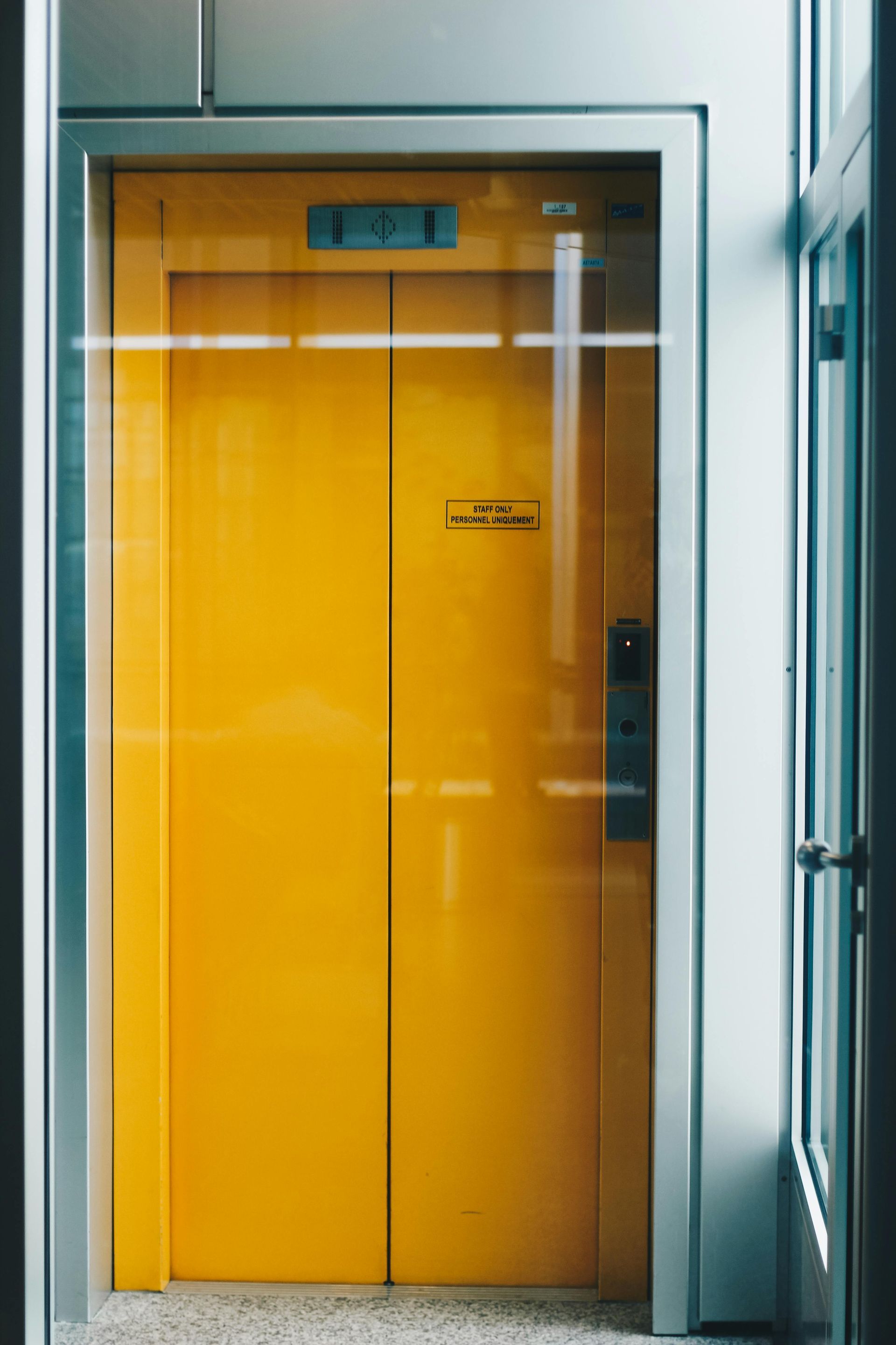 Yellow elevator doors in a building. Clear glass panels border the doors.