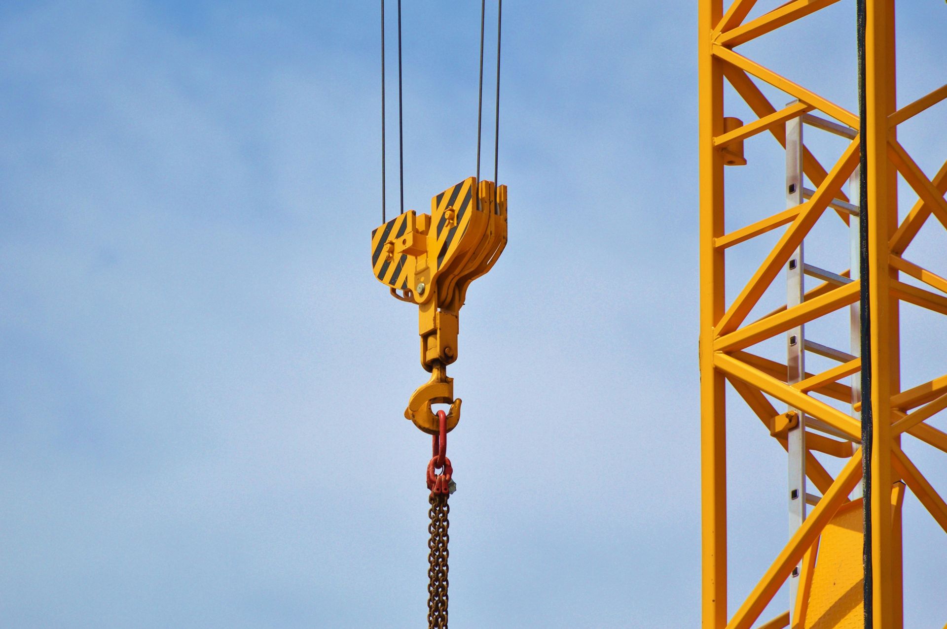 Yellow crane hook and chain against a blue sky, part of a construction crane.