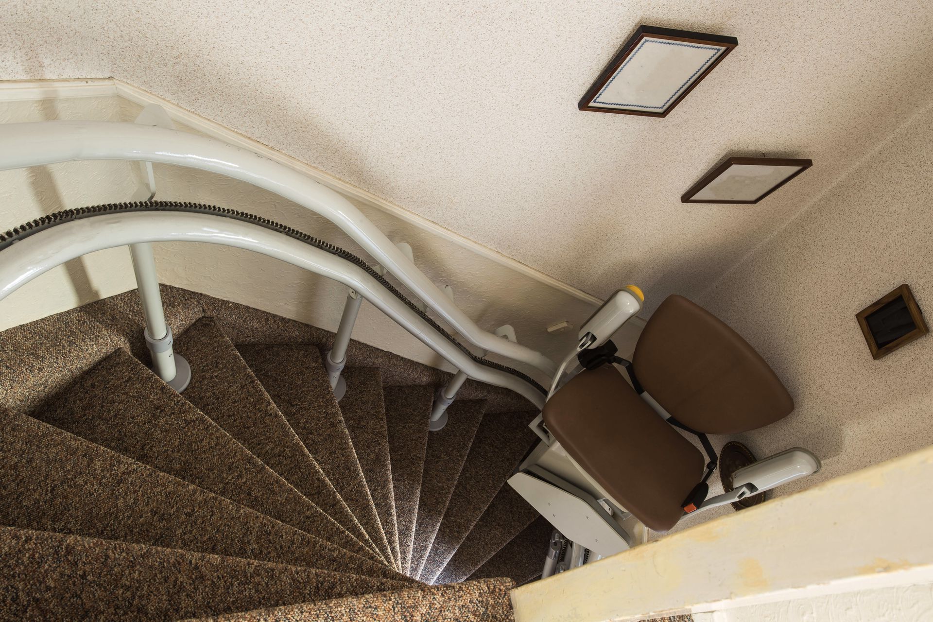 Stair lift installed on a curved staircase with brown carpet and a white handrail.